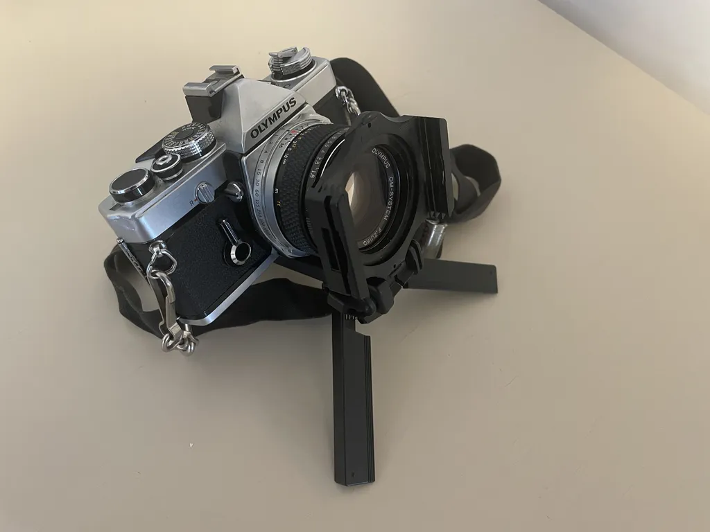 a black and silver metal camera on a tiny tripod. On the front of the lens is a black piece of plastic with ridged slots on either side of the lens