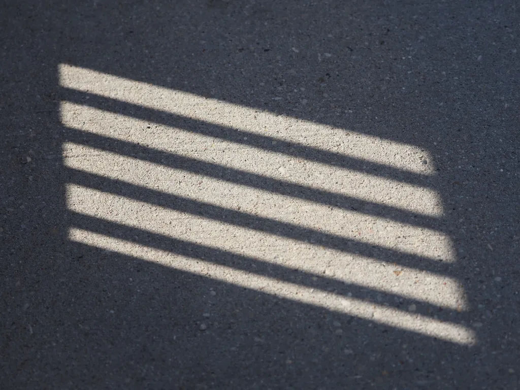 a shadow cast on a sidewalk from a hole in a fence