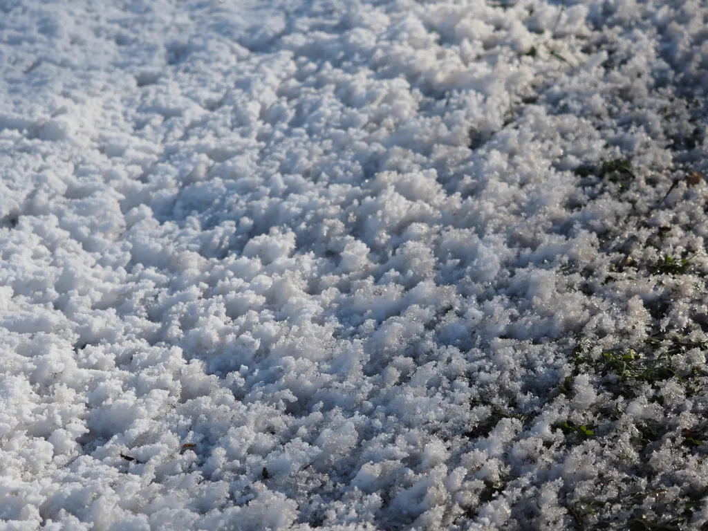 a berm covered in snow and ice that becomes sparser as it reaches the road