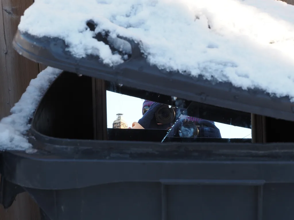 a selfie taken in fragments of mirror visible through a closed trash bin