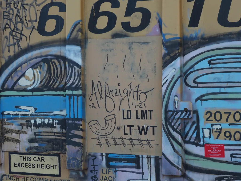 graffiti on a train car of a macaroni noodle next to a train track signed 'al freighto'