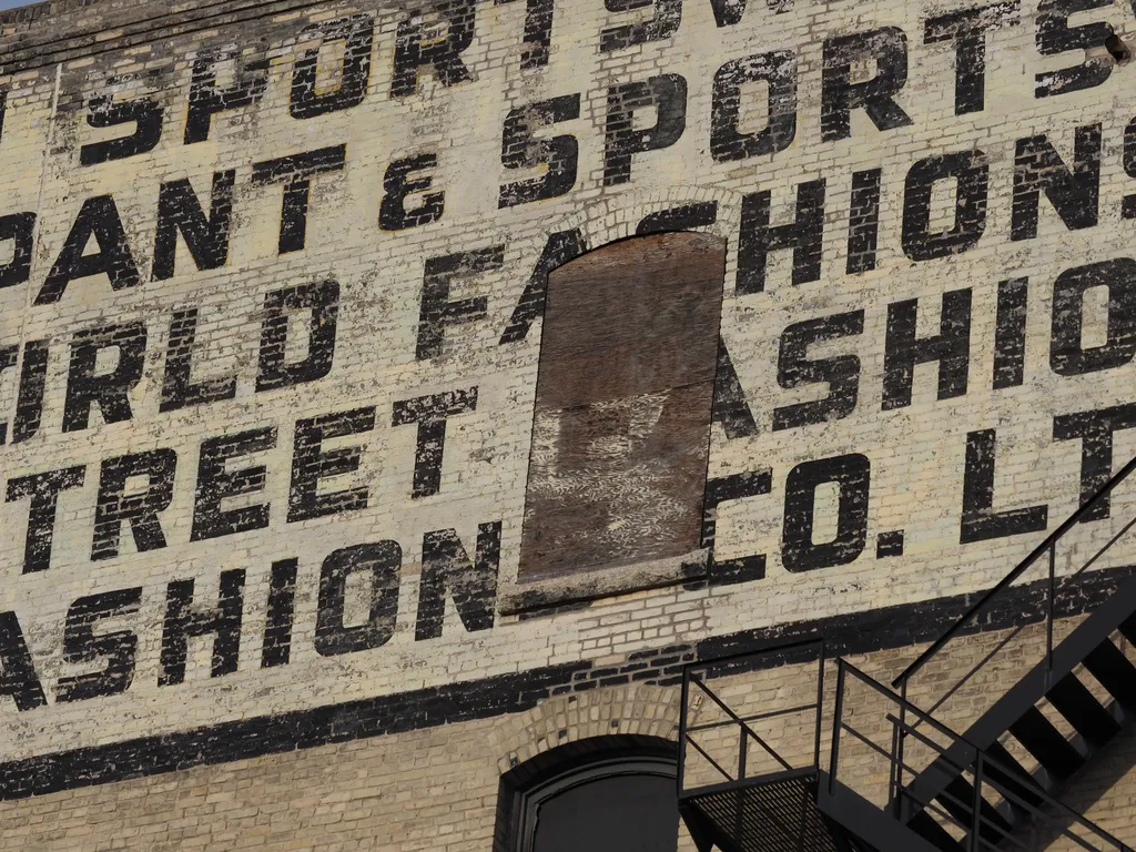 a boarded up window in the middle of an old advertisement painted onto a brick building