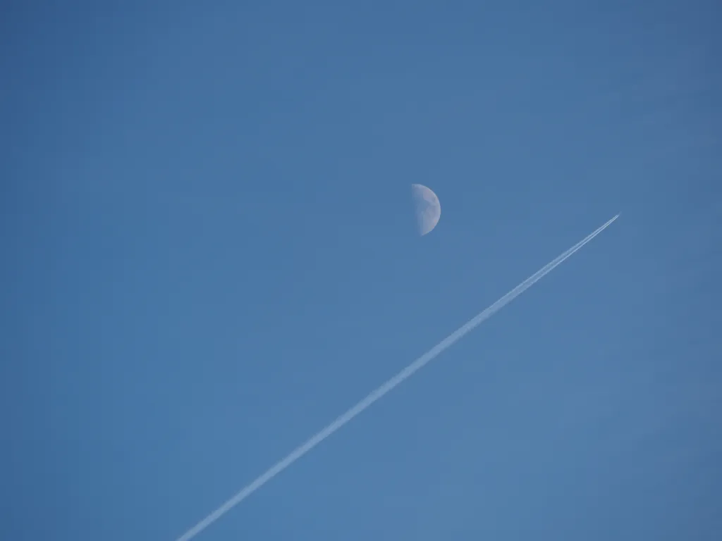 A jet flying by a quarter moon in a clear blue sky