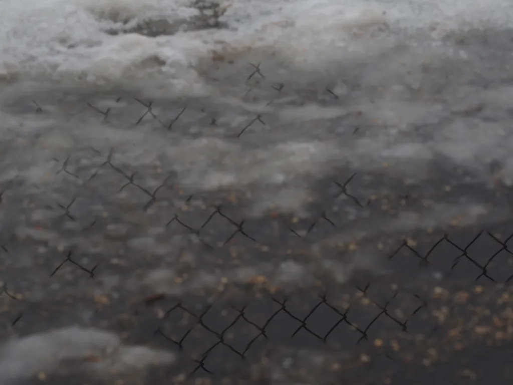 a chain-link fence reflected in an icy puddle