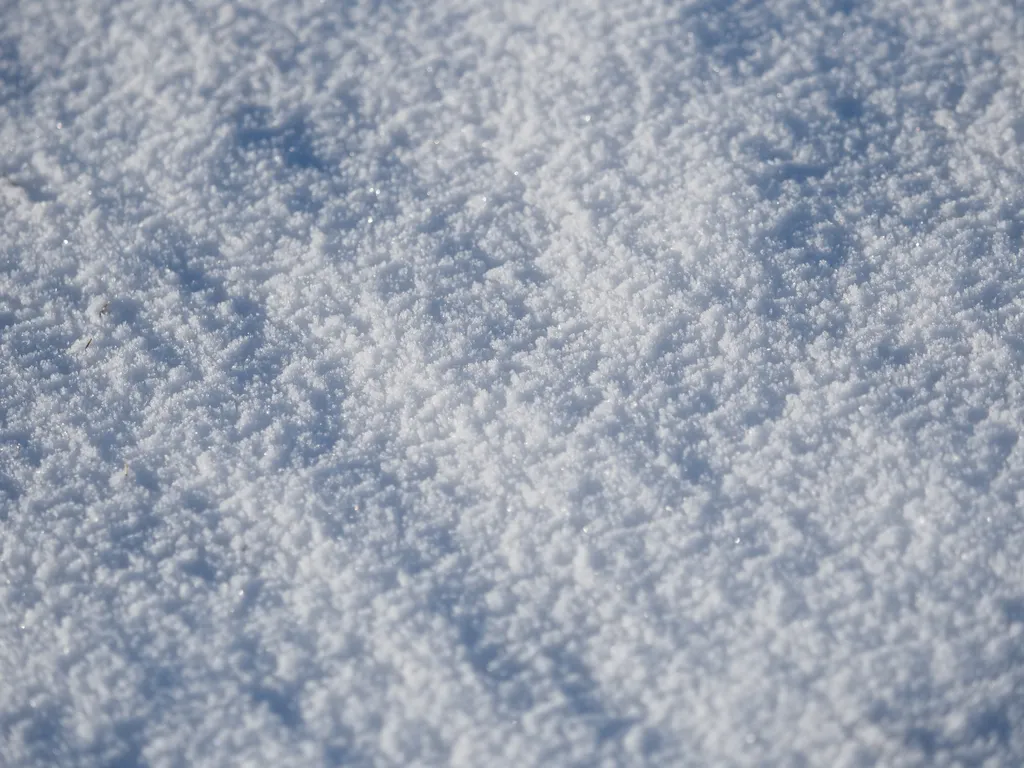 a close-up shot of snow in a field. the top of the snow has formed ice crystals, leaving a rough and slightly pitted surface