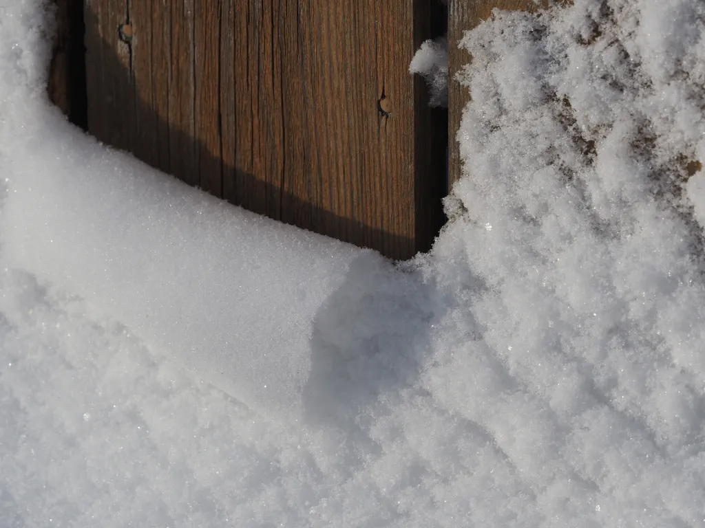 a sheet of snow along a fence that has started to curl over