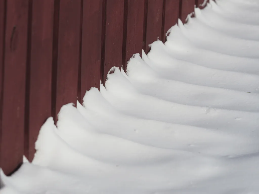 snow piling up along a fence