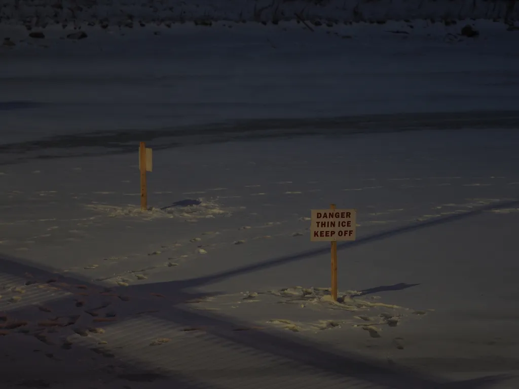 signs warning of thin ice on a frozen river