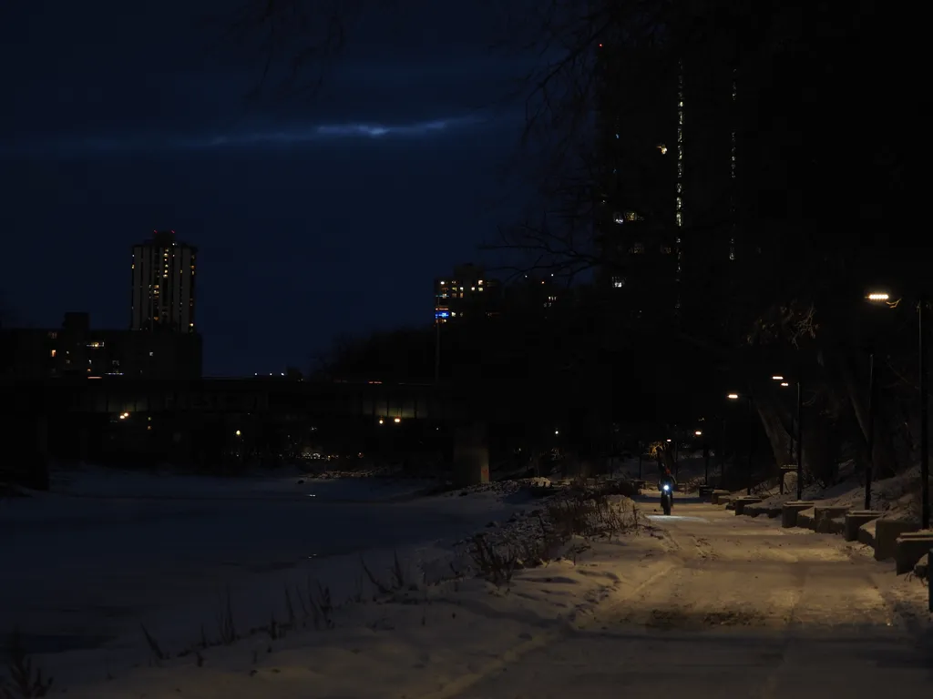 a bike rids down a snowy path beside a frozen river at night