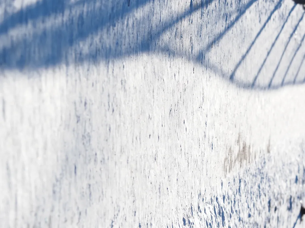 a chain-link fence casting a shadow on a sidewalk