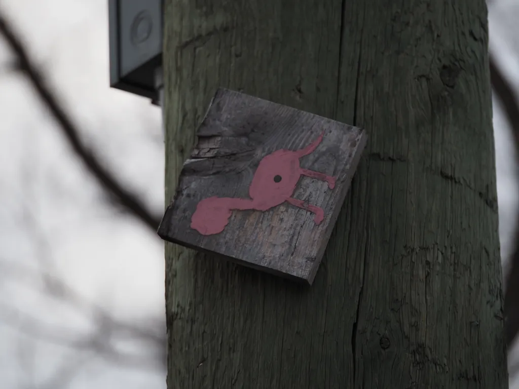 a pink quadruped painted onto a wooden block that is nailed to a utility pole