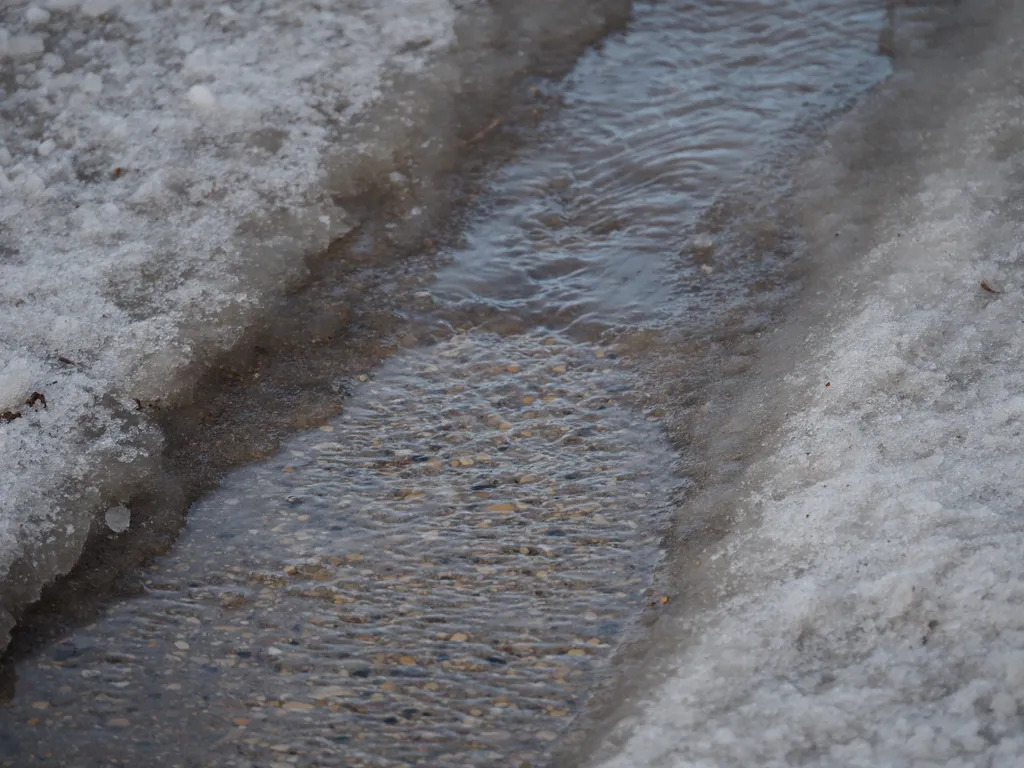 water rushing down the divot in a lante where cars have melted tracks in the ice