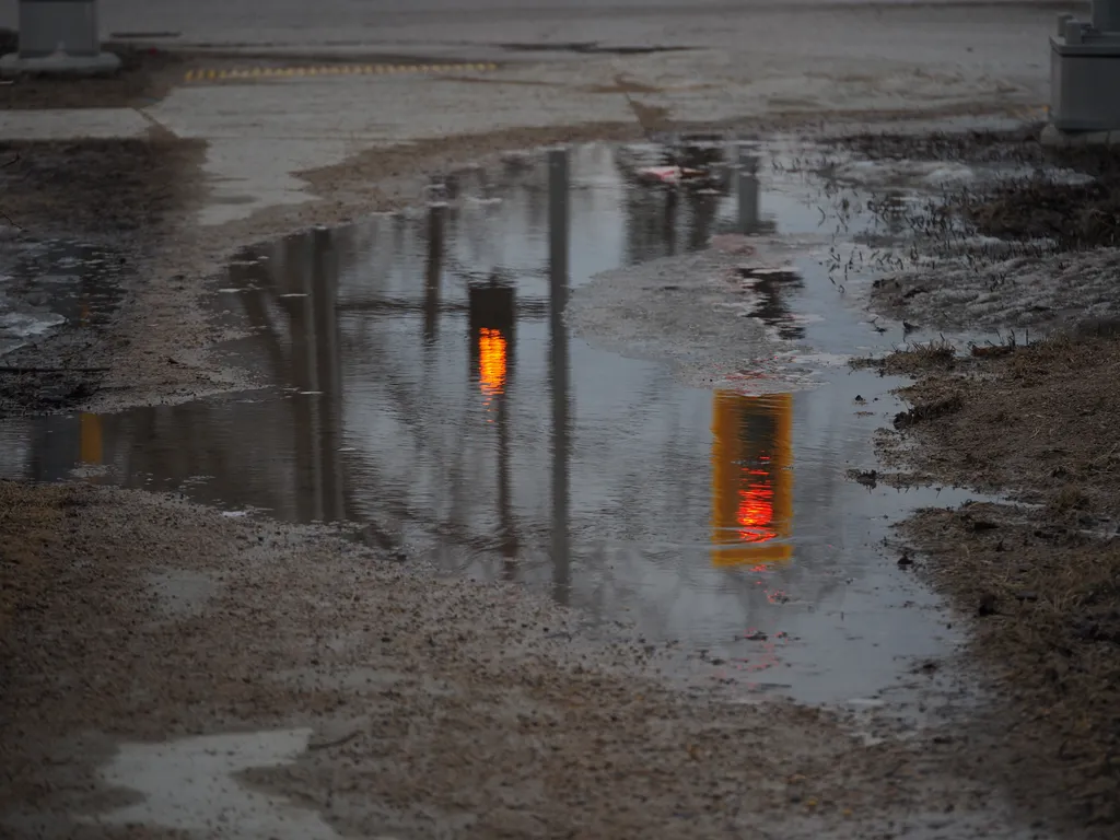 a stop light and a don't walk light reflected in a grimy puddle on a sidewalk