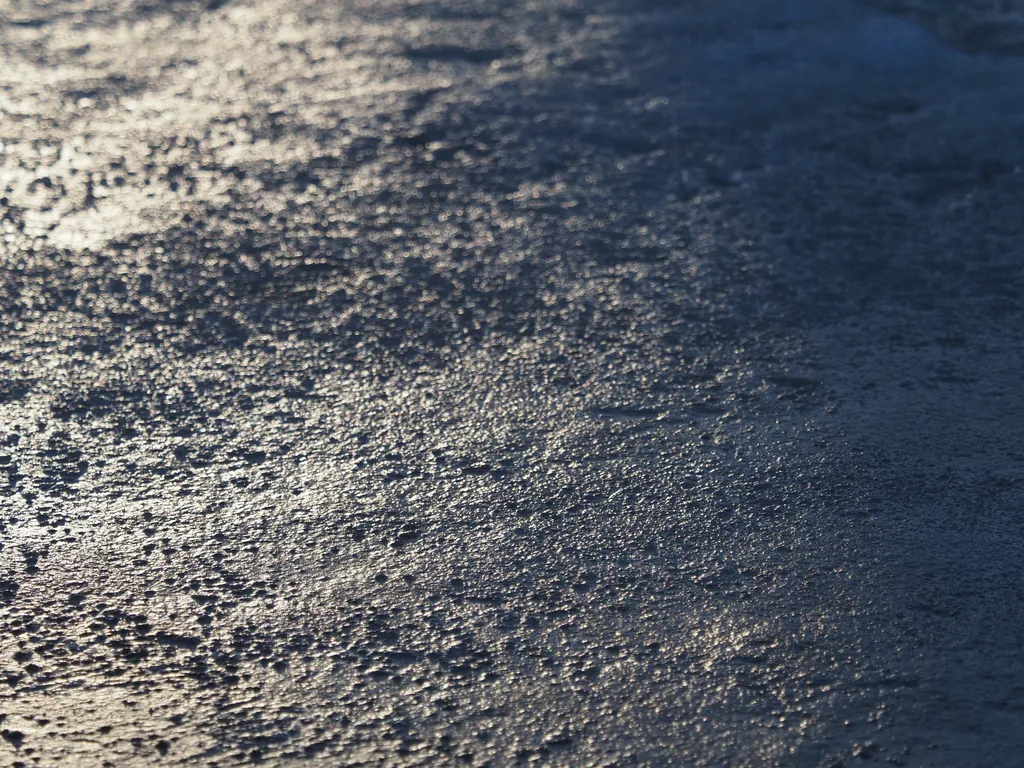 light reflecting on the mottled surface of a frozen puddle