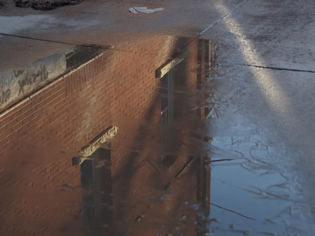 a brick building reflected in a frozen puddle