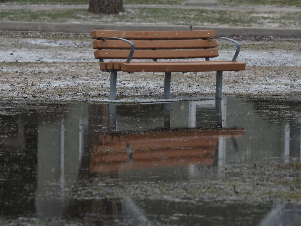 a park bench reflected in a snowy puddle