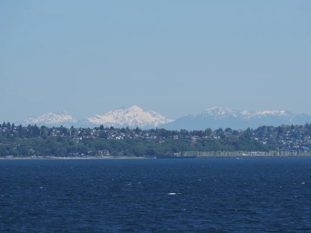 houses amidst trees between snow-capped mountains and choppy blue waves