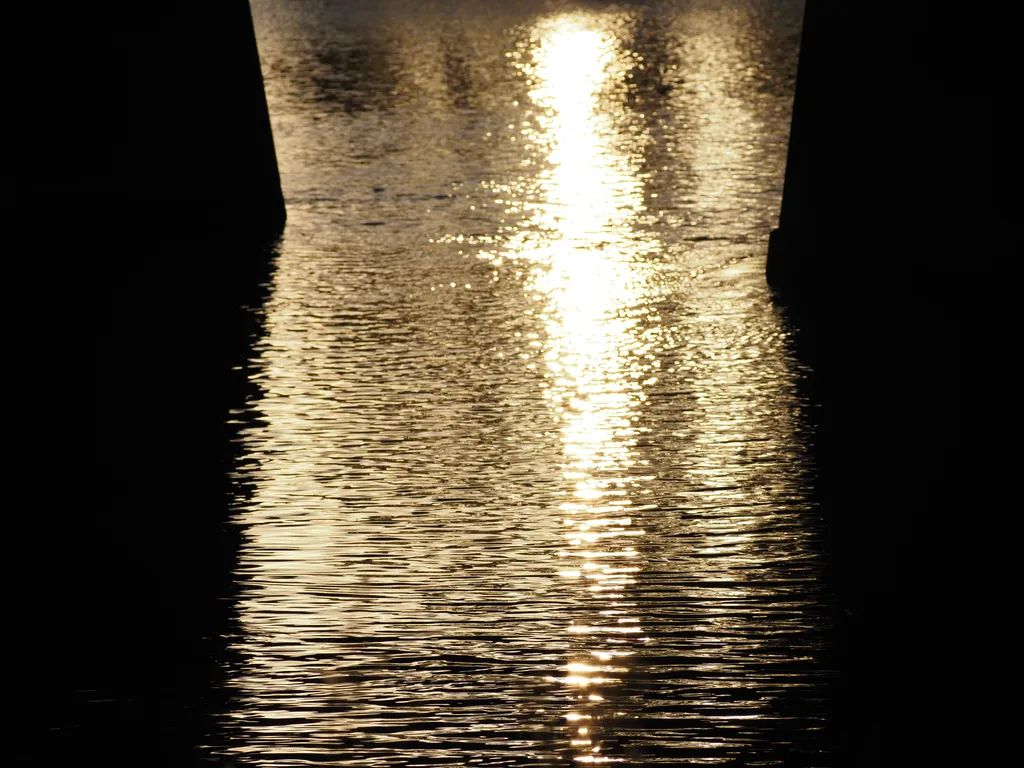 the sun reflecting on the river under a bridge