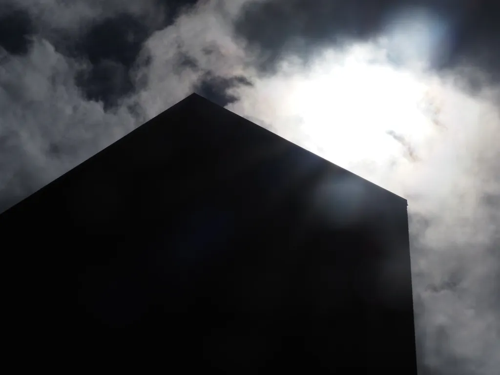 a tall brick building silhouetted against a bright sun in a cloudy sky