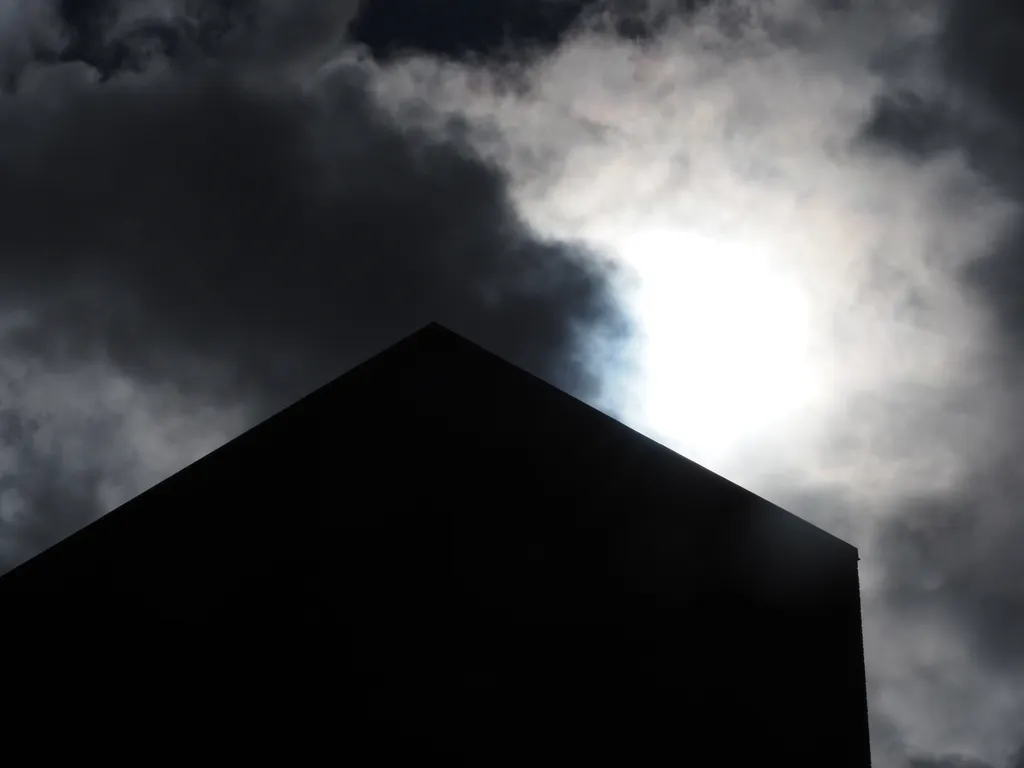 a tall brick building silhouetted against a bright sun in a cloudy sky