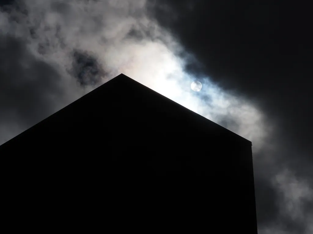 a tall brick building silhouetted against a bright sun in a cloudy sky