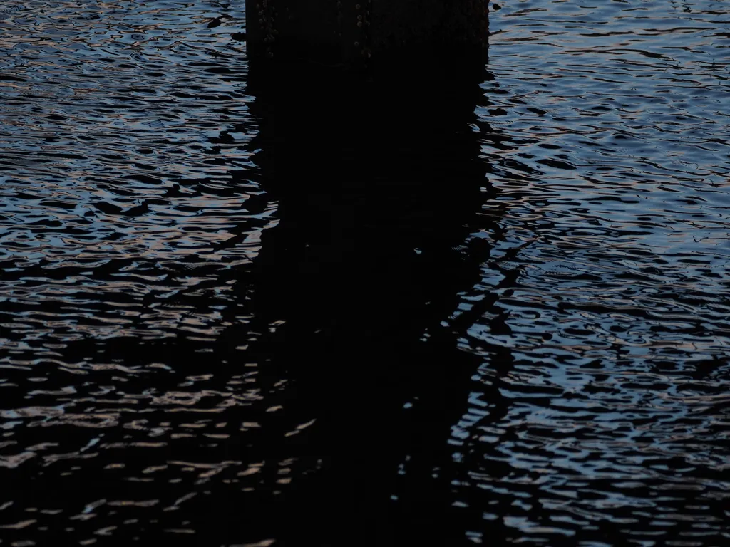 the sun reflecting on water under a pier