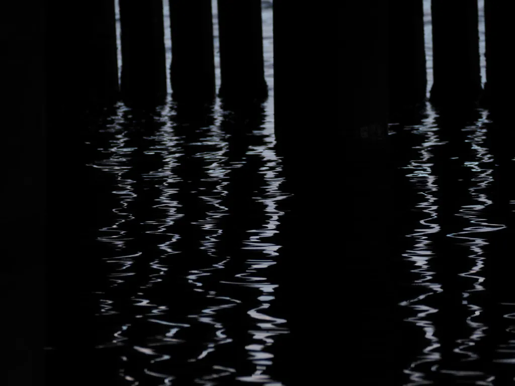 the sun reflecting on water under a pier