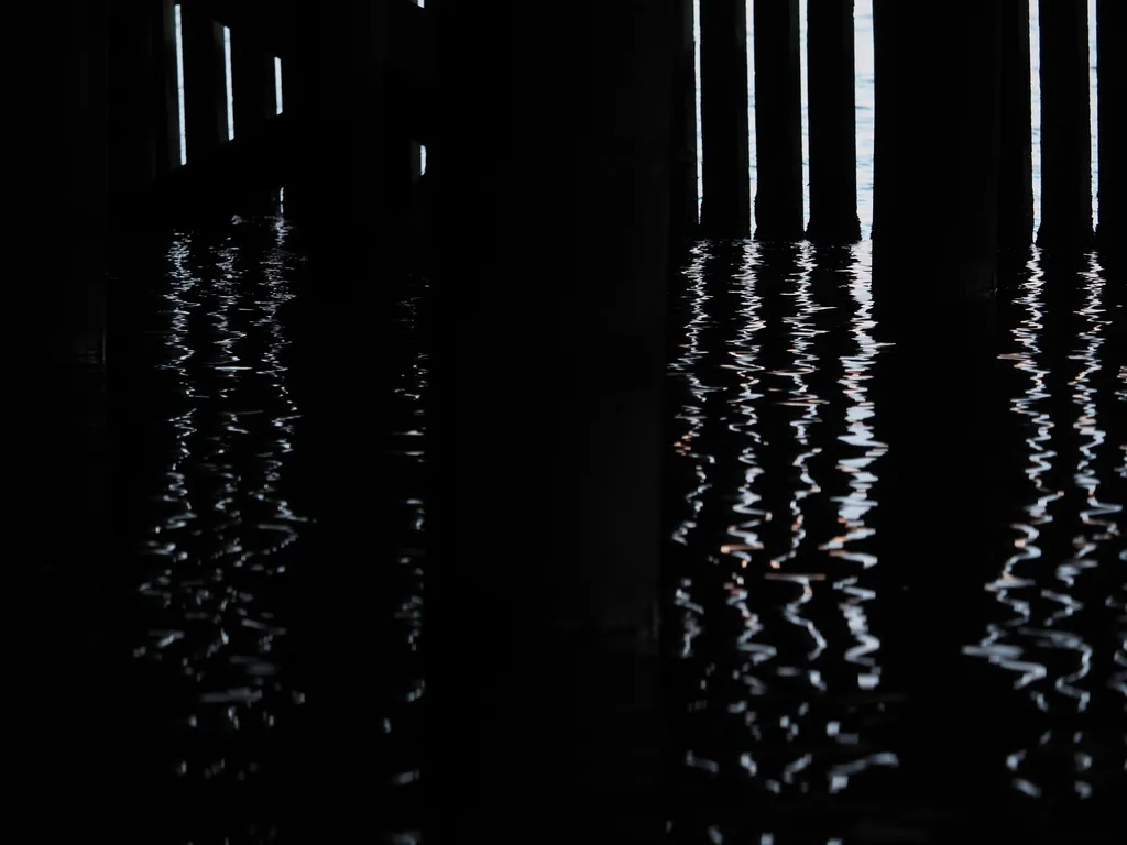 light reflecting on the water under a pier