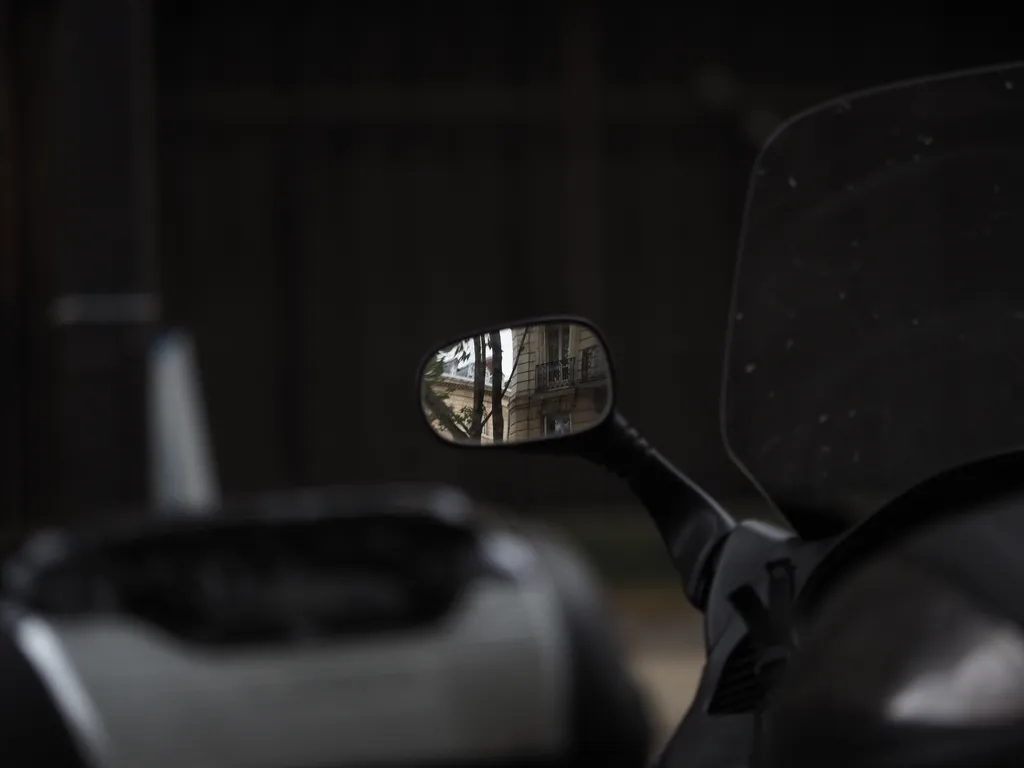 a building reflected in the mirror of a parked scooter