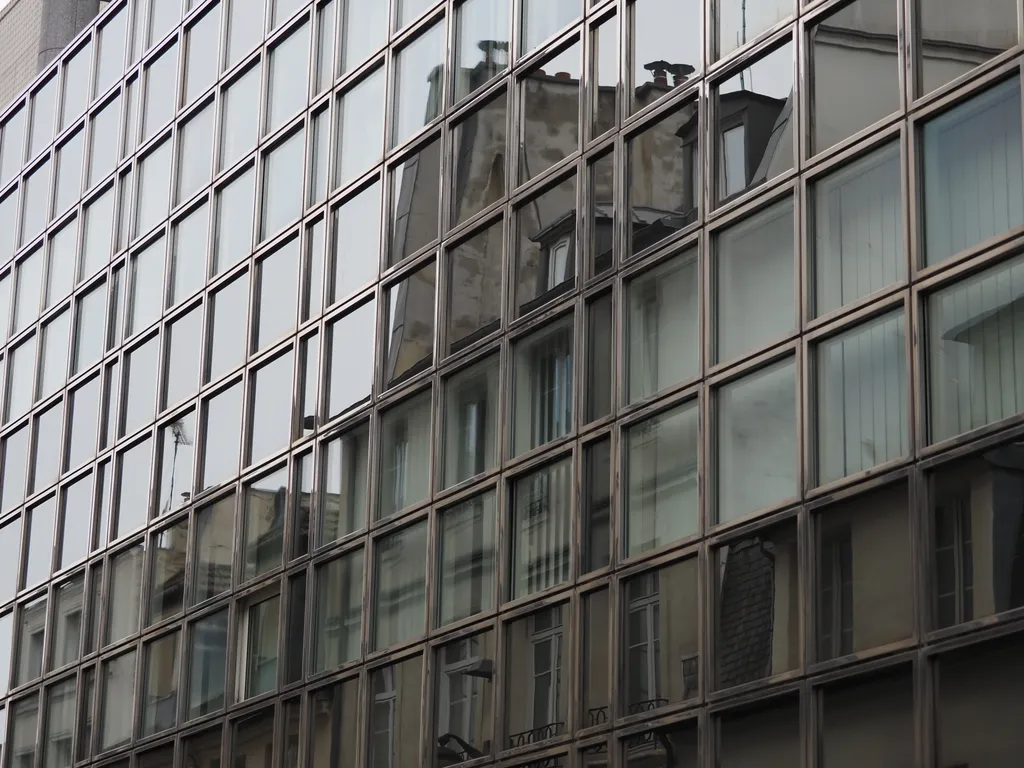 more traditional apartment buildings reflected in a sheer wall of square glass windows