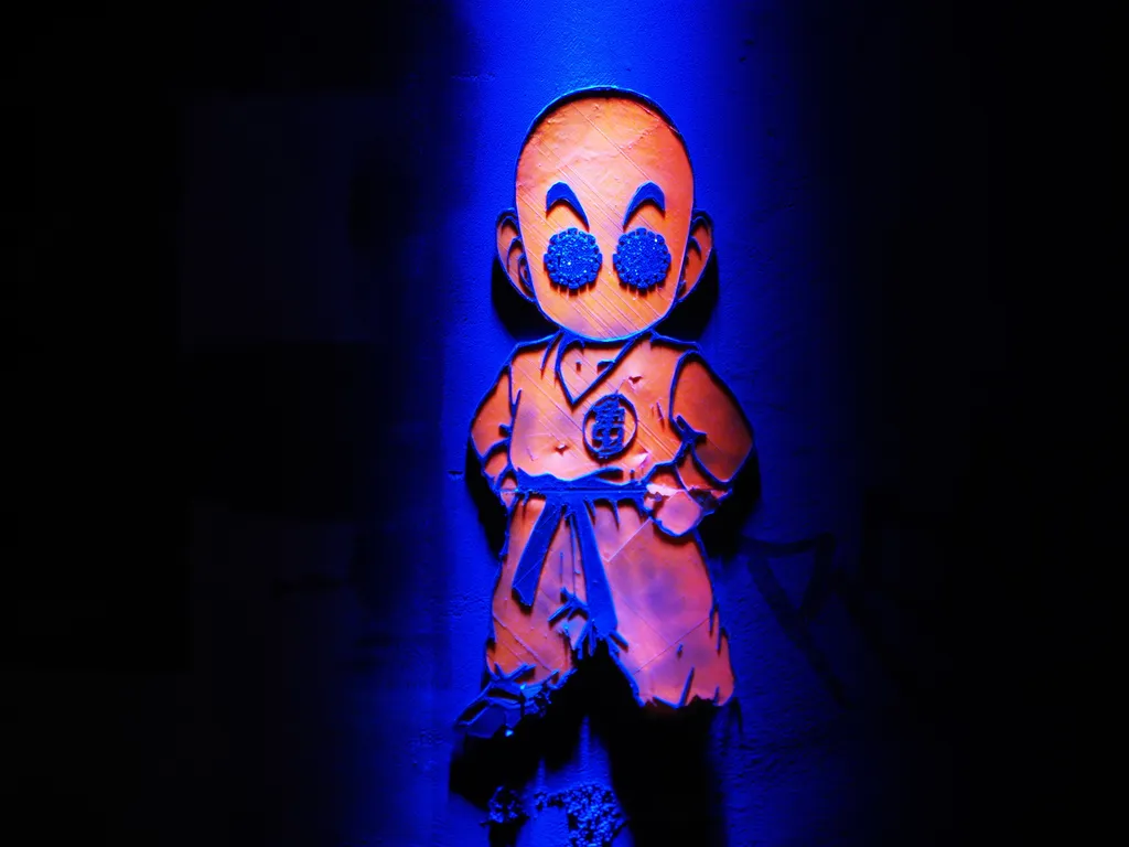 A sculpture of Krillin in his training gi bathed in blue light