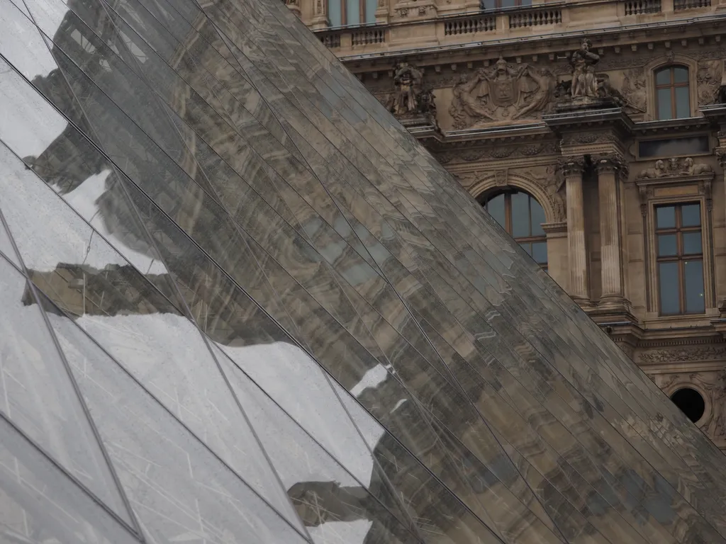 the glass pyramid of the louvre reflecting the louvre building beside it