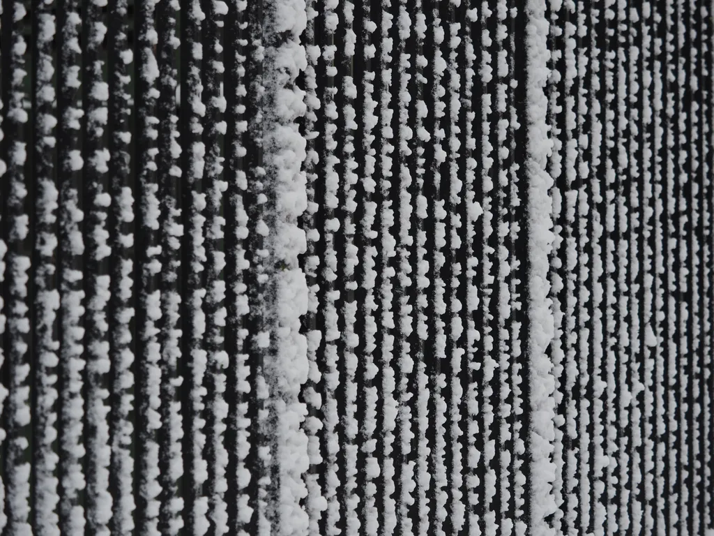 snow sticking to the side of the metal bars of a fence