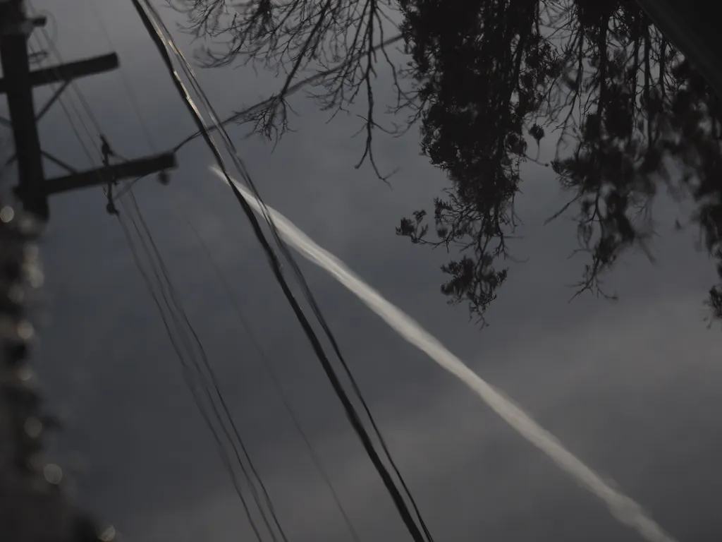 the contrail of a jet reflected in a puddle