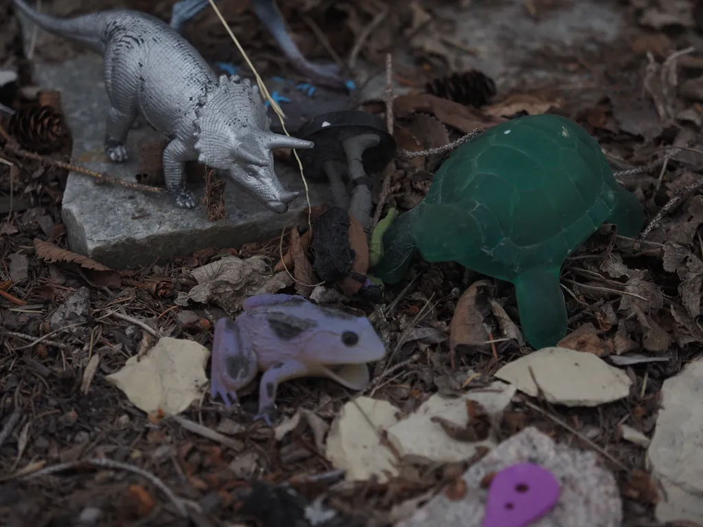 several plastic toys (a sea turtle, a triceratops, a frog, and a ninja turtle figurine) amidst fallen leaves and stones