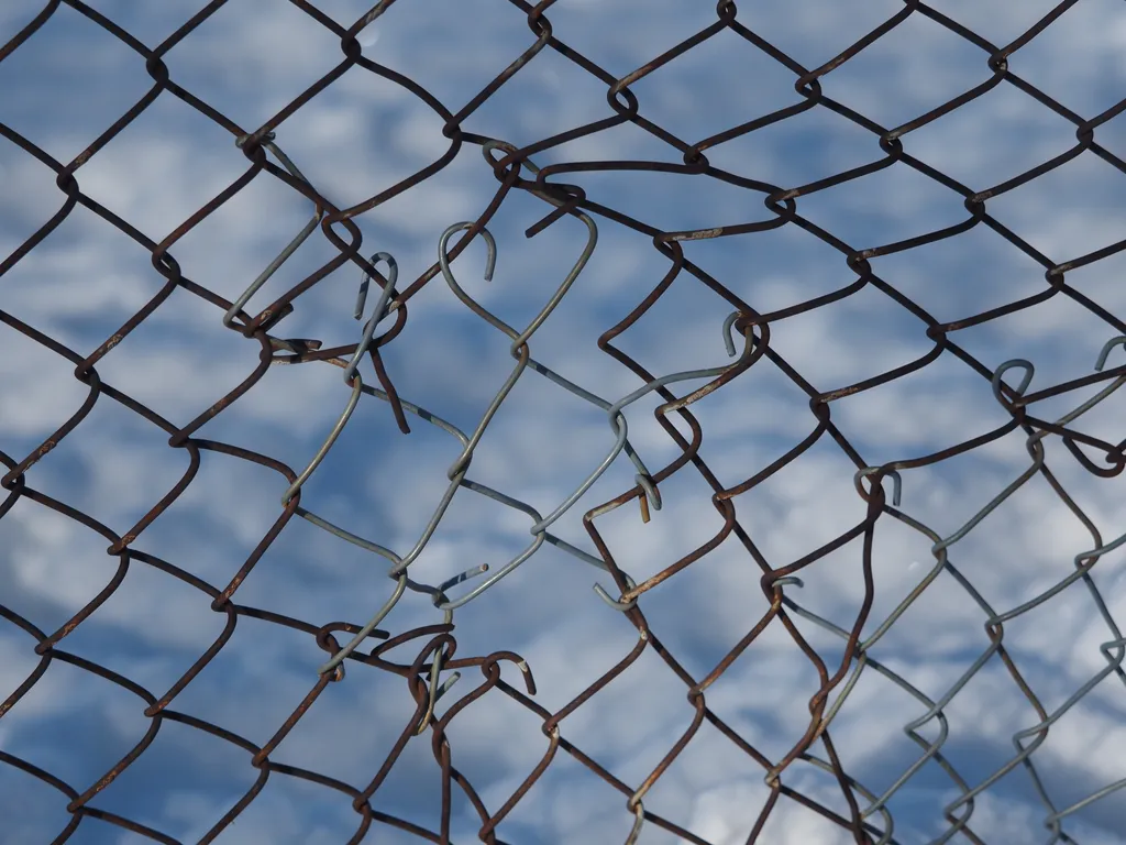 a chainlink fence that is bent where it was torn and then repared with new wires