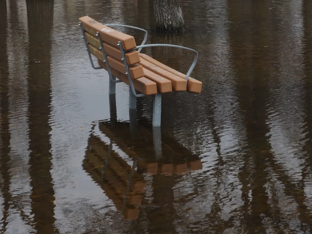 a park bench in a flooded field reflected in the water below it