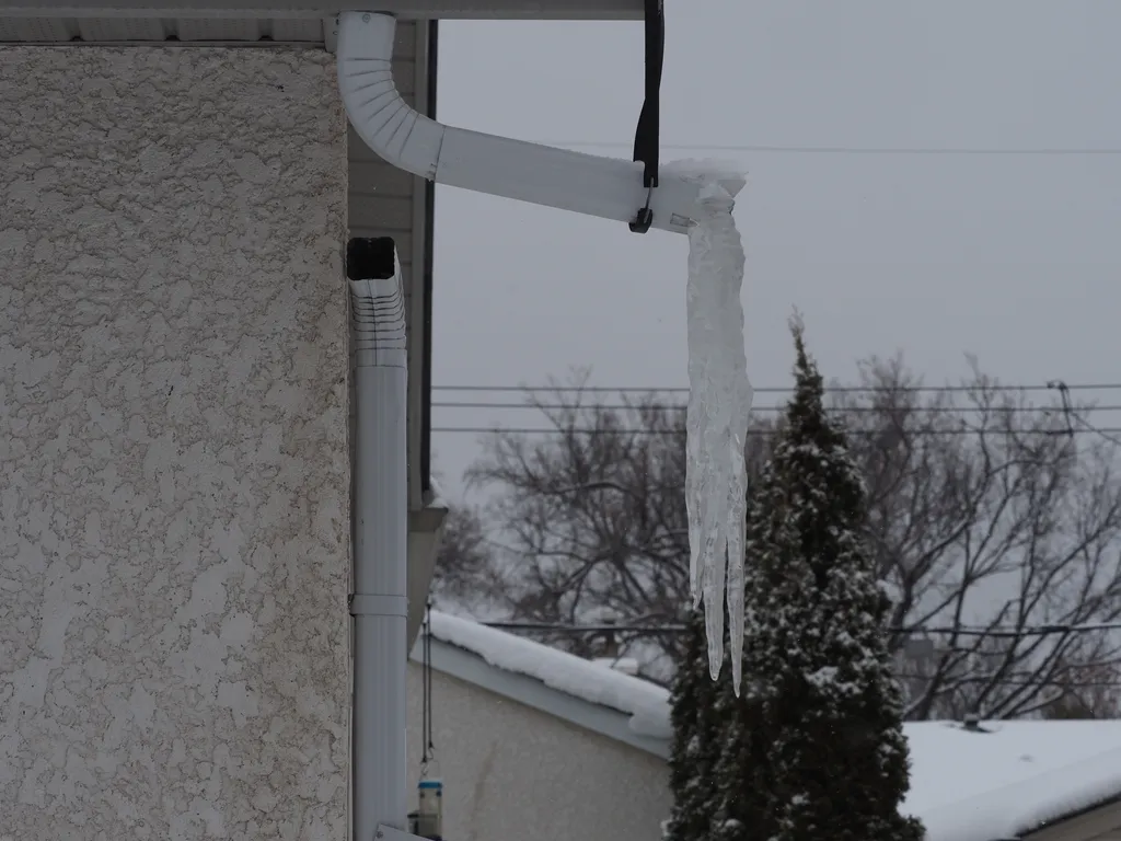 a long icicle hanging from a drainpipe that has become disconnected