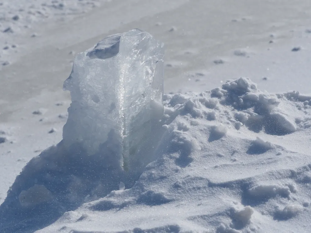 a block of ice in a snow drift on a path on a frozen river that is starting to dissapear under snow