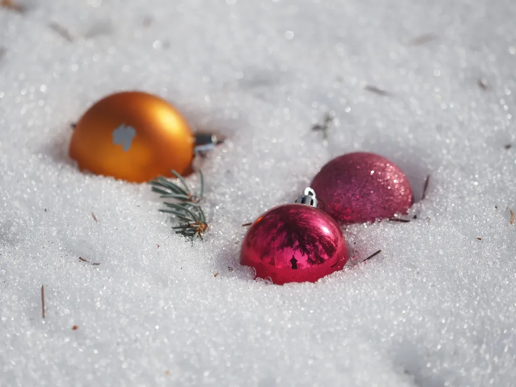 three round christmas baubles in moist snow. In the front bauble is a reflection of the photographer