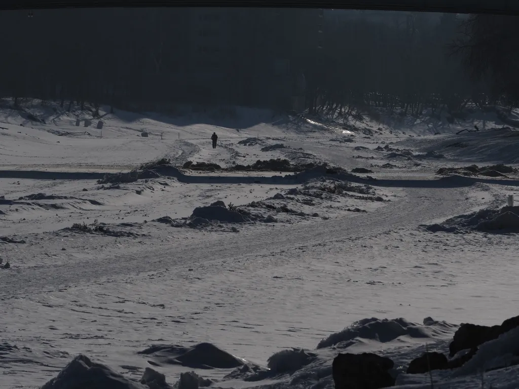 a lone person walks on a snowy path on a frozen river