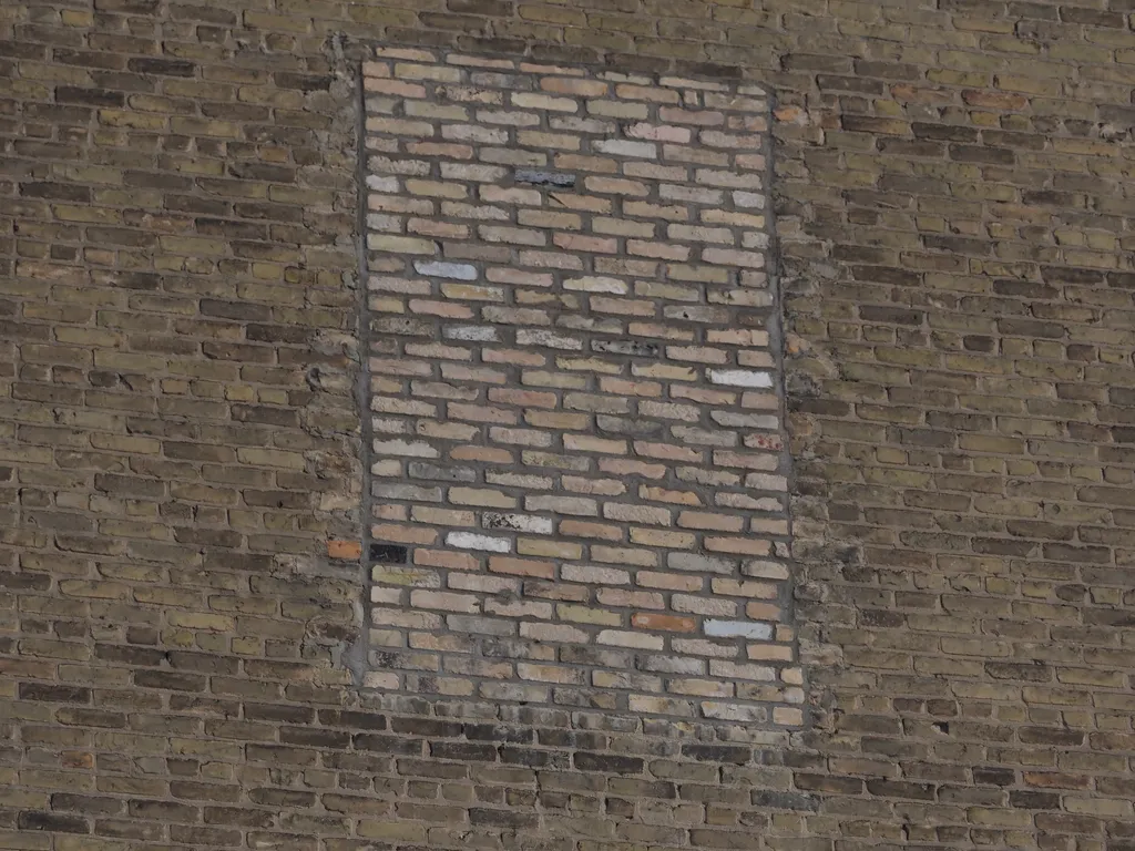 a brick wall with a square of differently-coloured bricks where a window was bricked up